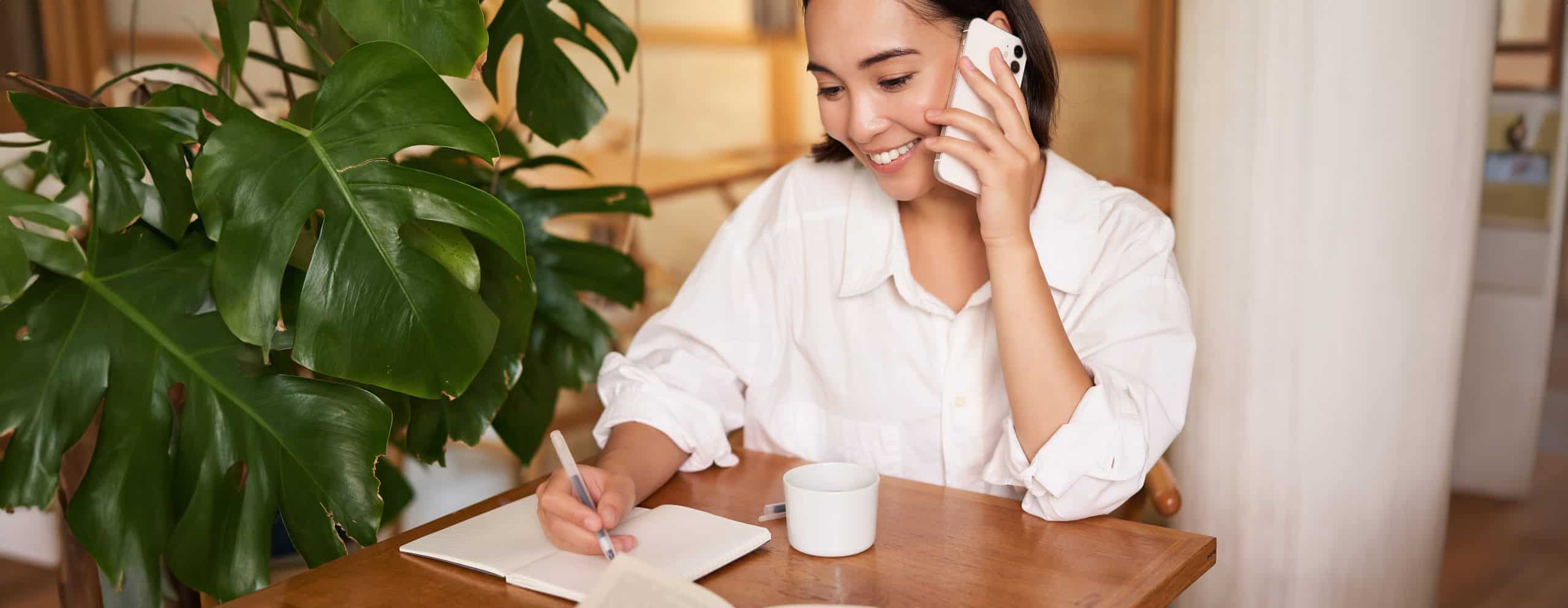 Working woman answer phone call in cafe, writing down, making notes while having conversation on telephone working-woman-answer-phone-call-cafe-writing-down-making-notes-while-having-phone-consultation